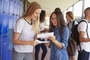 Happy teenage girls sharing exam results in school corridor