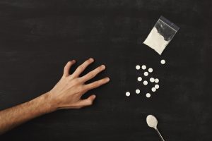 Man's hand reaching for drugs on dark table