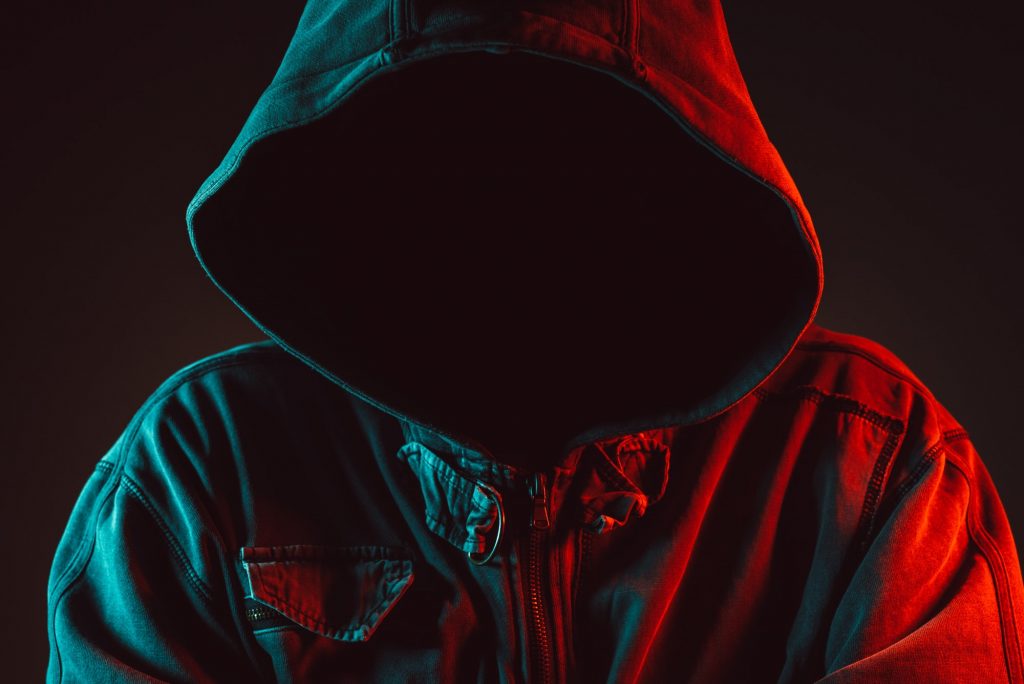 Red and blue lit low key portrait of hooded person